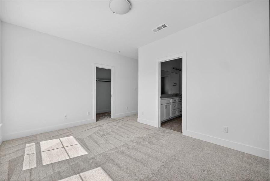 Unfurnished bedroom with a walk in closet, light carpet, and connected bathroom