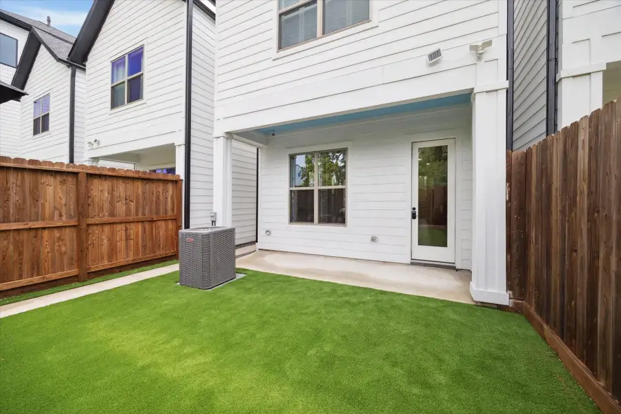 This photo showcases a compact backyard with grass, bordered by wooden fencing. It features a covered patio area with access through a glass door, providing a low-maintenance outdoor space.