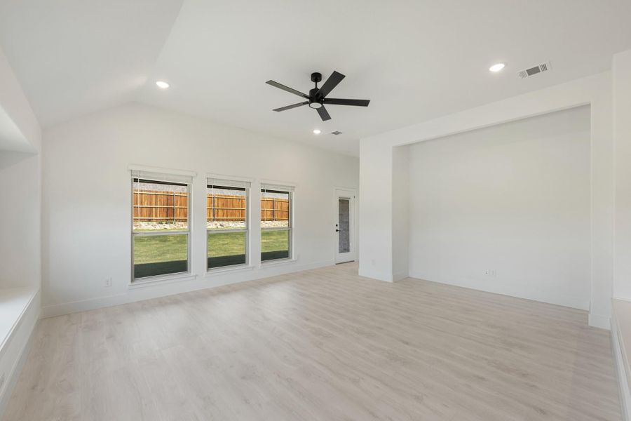 Empty living room with vaulted ceiling, black ceiling fan, light wood floors, and three backyard-facing windows