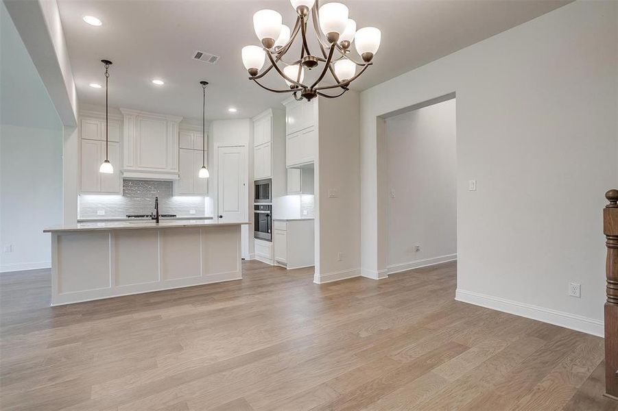 Kitchen featuring decorative light fixtures, a notable chandelier, light hardwood / wood-style floors, stainless steel appliances, and white cabinetry