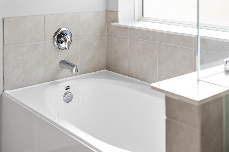 Indulge in the primary bath's deep, built-in soaking tub with elegant chrome fixtures and a sleek tile surround for a true spa-like retreat.