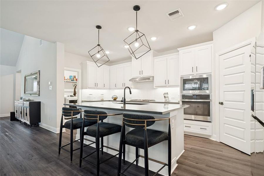Modern kitchen featuring an island with seating, white shaker cabinetry, stainless steel appliances, and dark wood-finish flooring