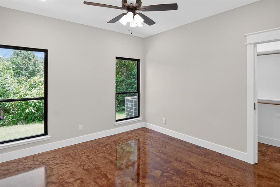 Bright room featuring two large windows with black framing, a ceiling fan, and concrete flooring Bright room featuring two large windows with black framing, a ceiling fan, and concrete flooring
