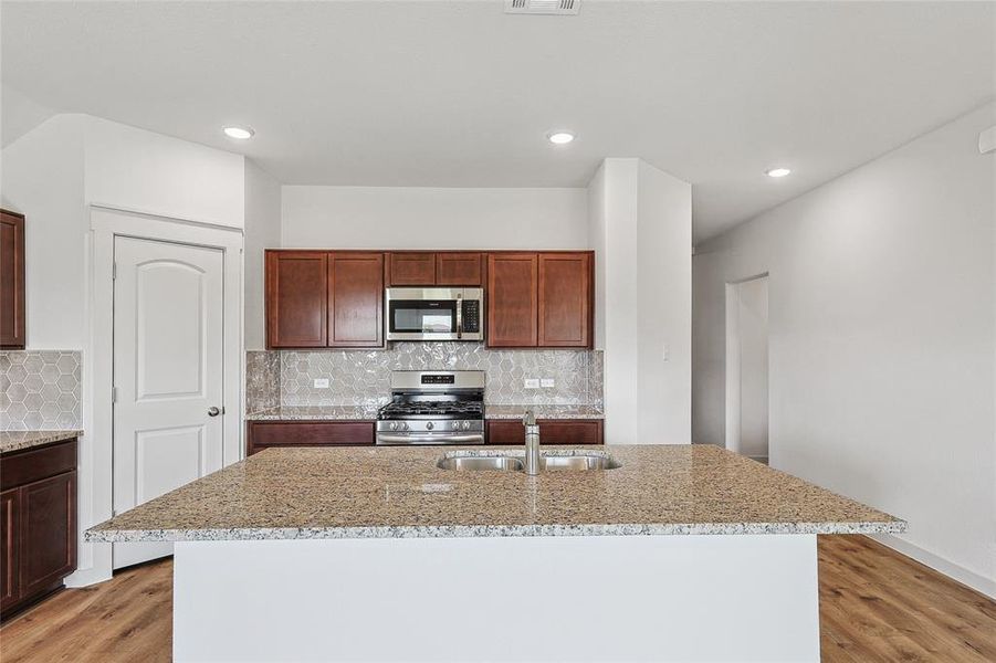 Kitchen featuring stainless steel appliances, light hardwood / wood-style floors, a center island with sink, and sink