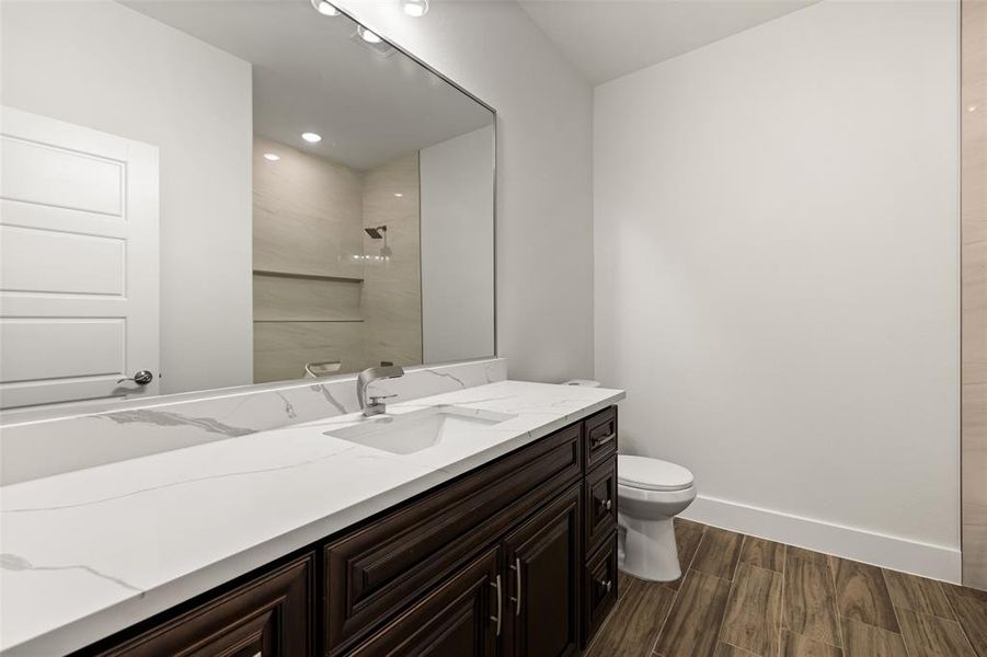 Bathroom featuring wood-type flooring, tiled shower, vanity, and toilet