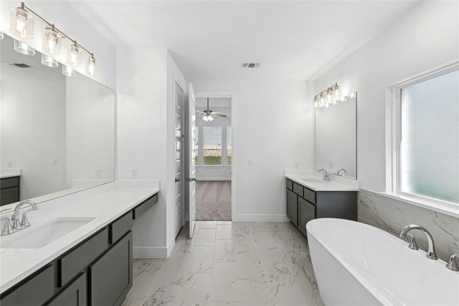 Bathroom featuring light marble finish floors, a freestanding bath, two vanities, a ceiling fan, and wainscoting