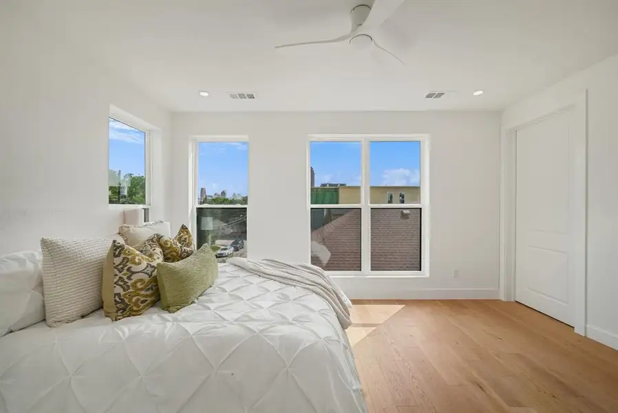 Bright bedroom featuring light wood-finish flooring and multiple windows Bright bedroom featuring light wood-finish flooring and multiple windows