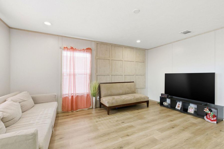 Living room featuring light wood-type flooring, recessed lighting, and a decorative wall