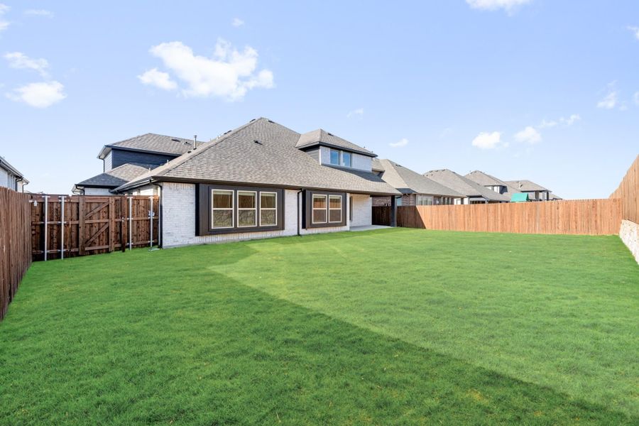 Backyard view of two-story home with brick exterior, large green lawn, and wood privacy fence Backyard view of two-story home with brick exterior, large green lawn, and wood privacy fence