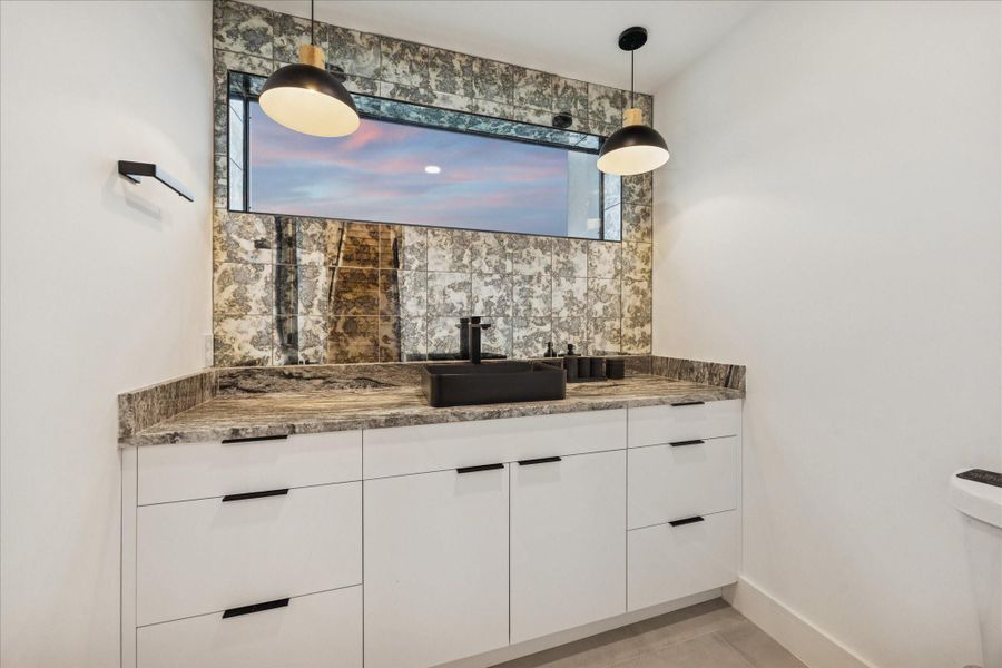 Second-floor powder bath showcasing a designer vanity with abundant storage, a striking stone countertop, modern matte-black fixtures, and statement pendant lighting.