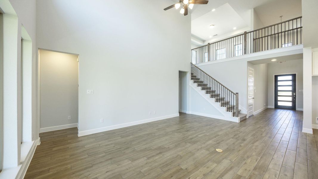 Unfurnished living room with a ceiling fan, a high ceiling, wood finished floors, and stairs Unfurnished living room with a ceiling fan, a high ceiling, wood finished floors, and stairs