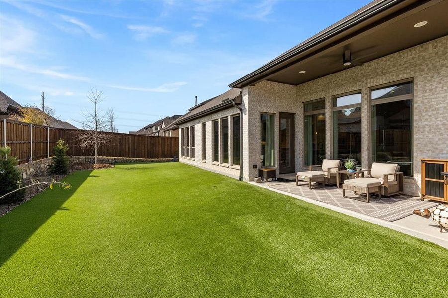 Low-maintenance backyard retreat featuring artificial turf, additional irrigated flower beds, trees, and an extended covered patio with ceiling fan.