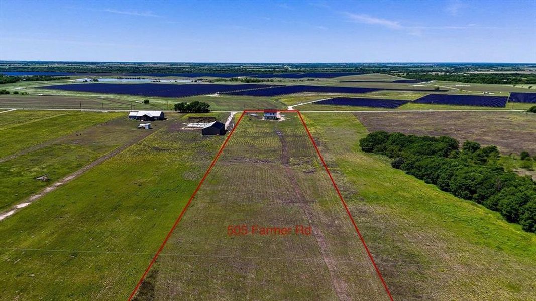 Expansive agricultural land featuring a white single-story home with a red roof, multiple outbuildings, and mature trees