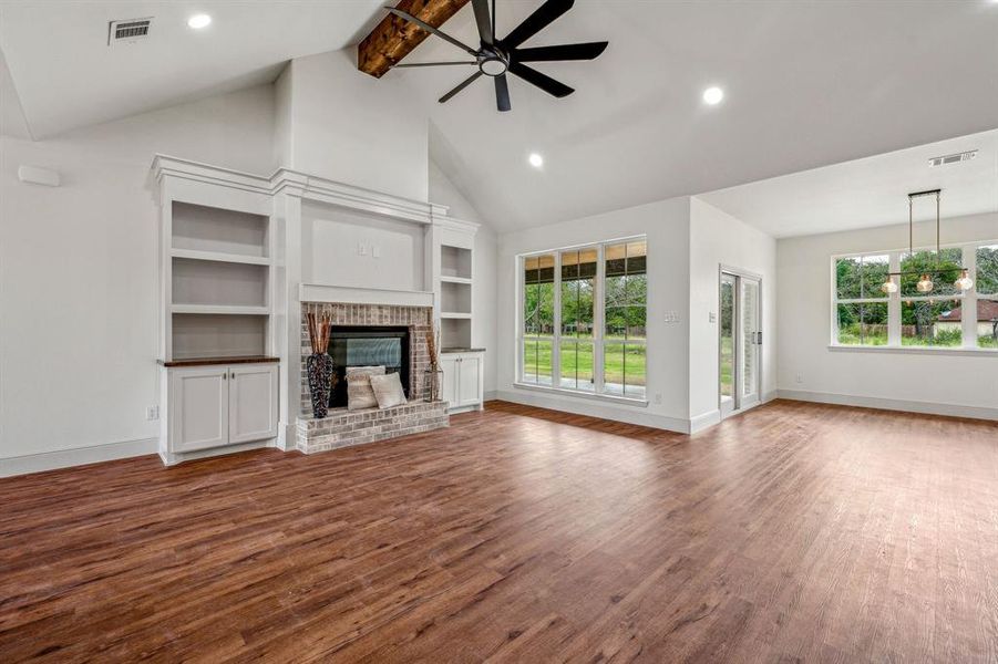 Unfurnished living room with beamed ceiling, hardwood / wood-style floors, a fireplace, a healthy amount of sunlight, and ceiling fan