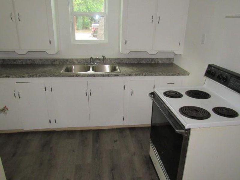 Kitchen with white range with electric stovetop, white cabinetry, dark wood-style flooring, and dark countertops Kitchen with white range with electric stovetop, white cabinetry, dark wood-style flooring, and dark countertops