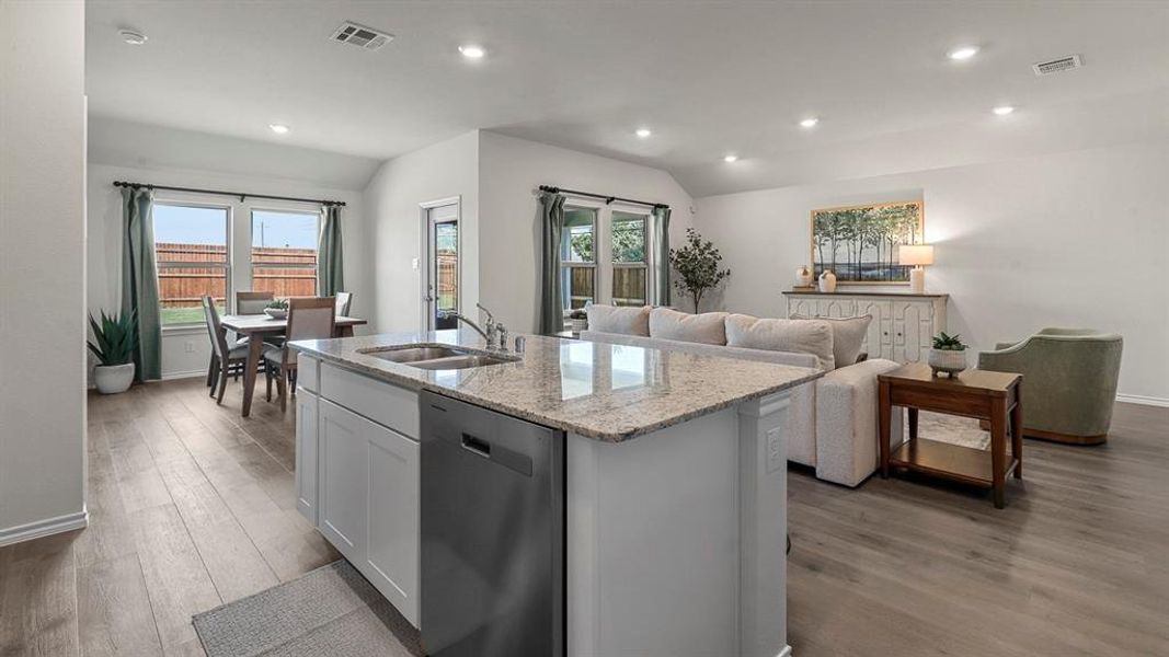 The open-concept living area features light wood-look flooring, recessed lighting, and a kitchen island with a granite countertop and stainless steel sink