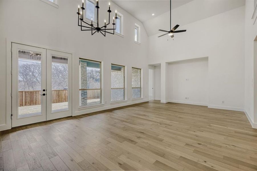 Unfurnished living room with hanging lights, light wood-type flooring, lofted ceiling, ceiling fan, and french doors