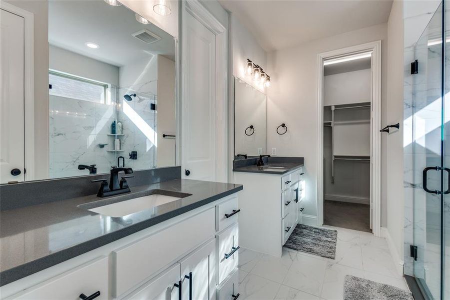 Bathroom featuring a marble finish shower, a walk in closet, two vanities, and light marble finish flooring