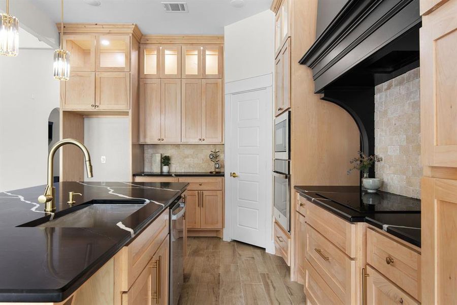 Kitchen featuring light hardwood / wood-style flooring, an island with sink, decorative backsplash, hanging light fixtures, and custom range hood