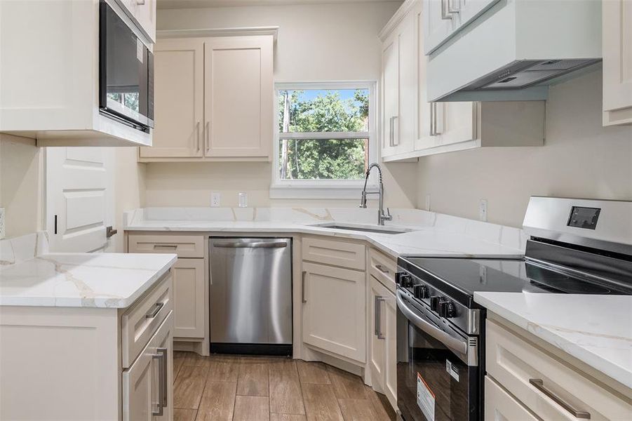 Kitchen featuring light cabinetry, stainless steel appliances, white countertops, and wood-finish flooring Kitchen featuring light cabinetry, stainless steel appliances, white countertops, and wood-finish flooring