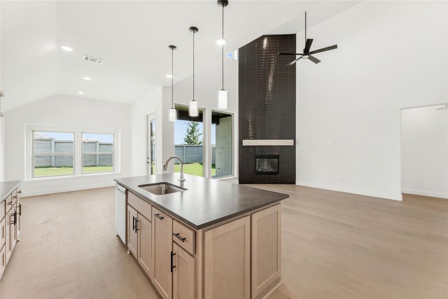 Open-concept kitchen and living area with center island, dark tile fireplace, vaulted ceiling, and light wood floors