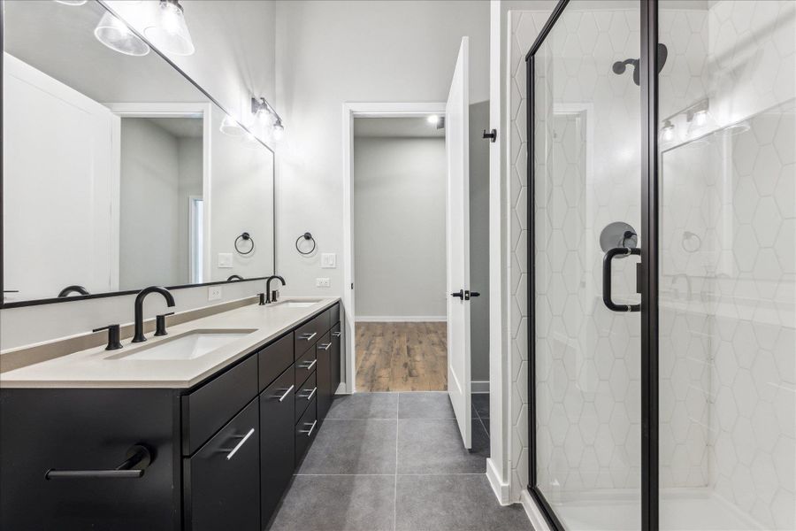 A well-lit primary bathroom features a dual vanity, sleek dark cabinetry, and a spacious glass-enclosed shower. A well-lit primary bathroom features a dual vanity, sleek dark cabinetry, and a spacious glass-enclosed shower.