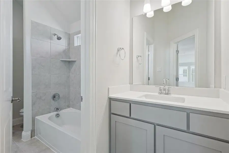 Bathroom featuring vanity, washtub / shower combination, light tile patterned floors, and vaulted ceiling Bathroom featuring vanity, washtub / shower combination, light tile patterned floors, and vaulted ceiling