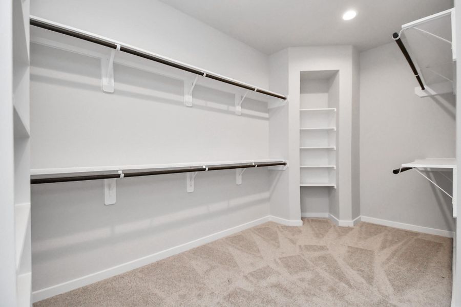 Spacious walk-in closet with high ceilings and plush carpet. Warm paint tones, built-in shelving, and dark finishes create a contemporary and functional retreat. Sample photo of completed home with similar floor plan. Actual colors and selections may vary. Spacious walk-in closet with high ceilings and plush carpet. Warm paint tones, built-in shelving, and dark finishes create a contemporary and functional retreat. Sample photo of completed home with similar floor plan. Actual colors and selections may vary.