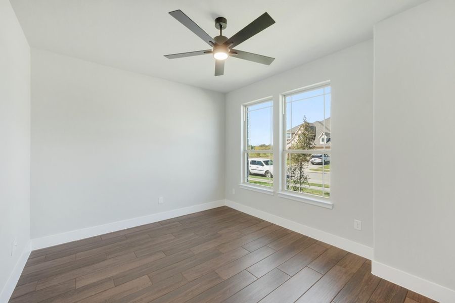 Empty room with dark hardwood floors, ceiling fan, and two windows overlooking a neighborhood street. Empty room with dark hardwood floors, ceiling fan, and two windows overlooking a neighborhood street.