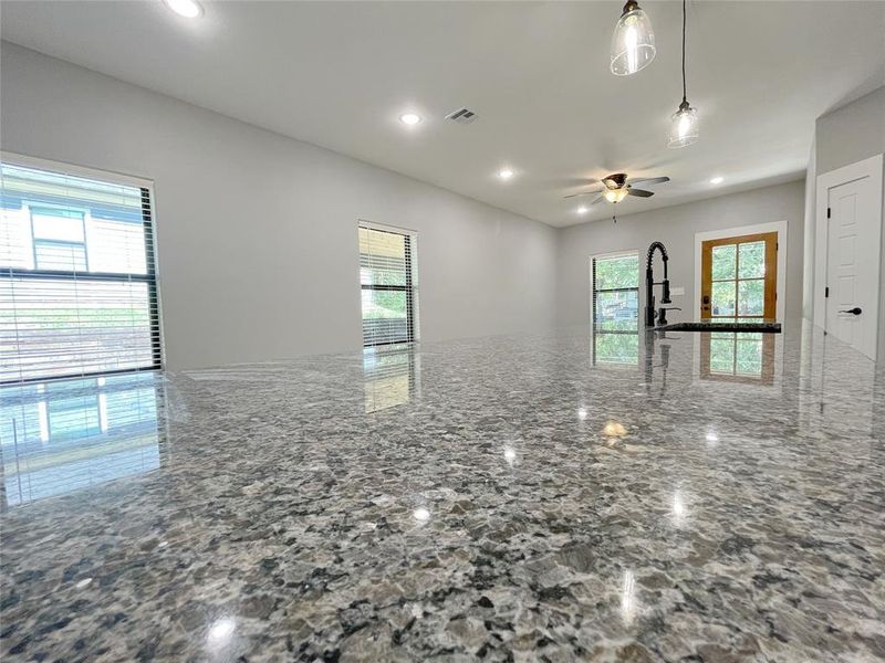 Kitchen with ceiling fan, hanging light fixtures, and stone counters