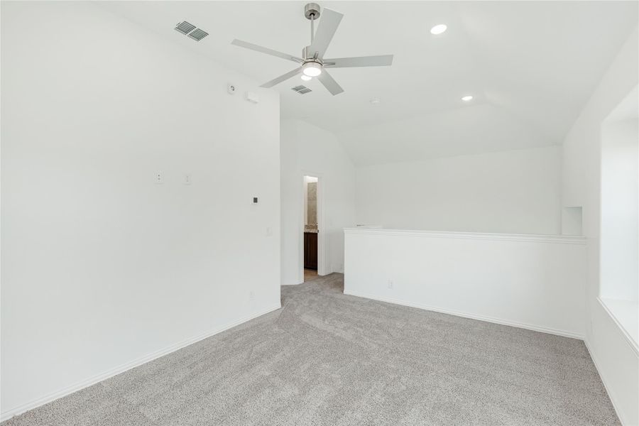 Empty bedroom with vaulted ceiling, ceiling fan, gray carpet, and ensuite bathroom doorway visible Empty bedroom with vaulted ceiling, ceiling fan, gray carpet, and ensuite bathroom doorway visible