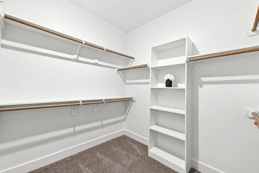Spacious primary walk-in closet featuring multiple hanging areas and built-in shelving, offering generous storage and organization space. Spacious primary walk-in closet featuring multiple hanging areas and built-in shelving, offering generous storage and organization space.