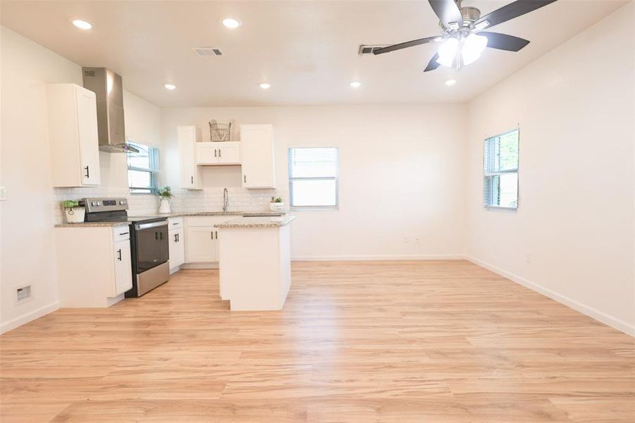 Kitchen with stainless steel range with electric cooktop, wall chimney range hood, a kitchen island, healthy amount of natural light, and recessed lighting