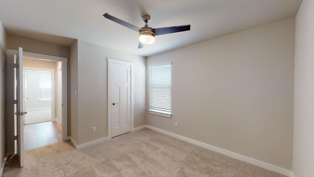 A well-lit bedroom features plush carpeting and a modern ceiling fan, offering comfortable living. A well-lit bedroom features plush carpeting and a modern ceiling fan, offering comfortable living.