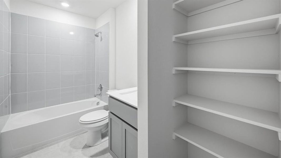 Bathroom featuring a white tub, shower with light gray tile surround, sleek vanity with a rectangular sink, and built-in shelving