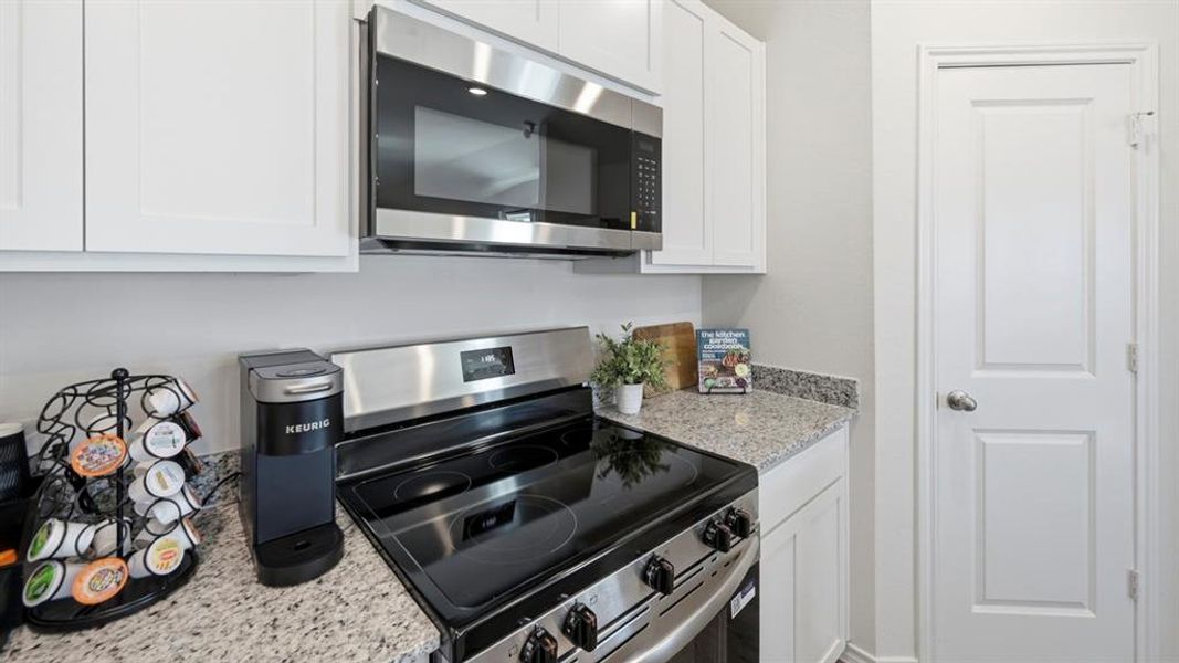 The kitchen features white cabinetry, granite countertops, and stainless steel appliances including a microwave and range