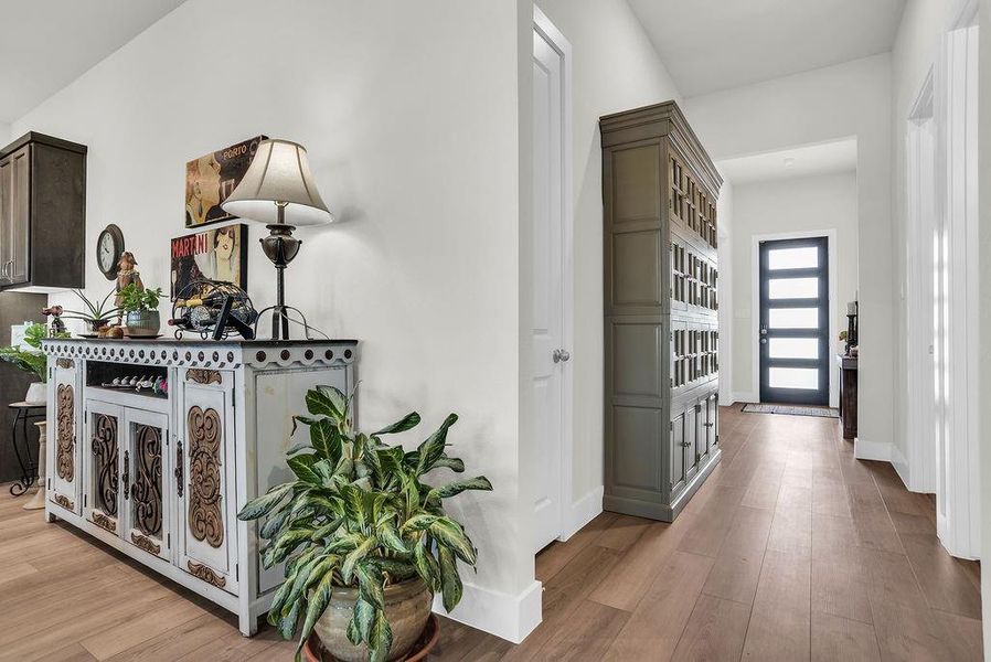 Modern entry door featuring frosted glass insets flooding the room with natural light, wood-finish flooring, and white trim throughout open to the study.