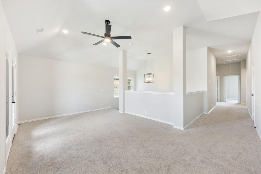 Open living area with vaulted ceiling, ceiling fan, carpet floors, and hallway leading to bedrooms
