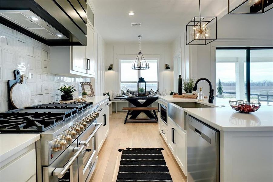 Kitchen with appliances with stainless steel finishes, white cabinetry, custom range hood, pendant lighting, and light wood finished floors