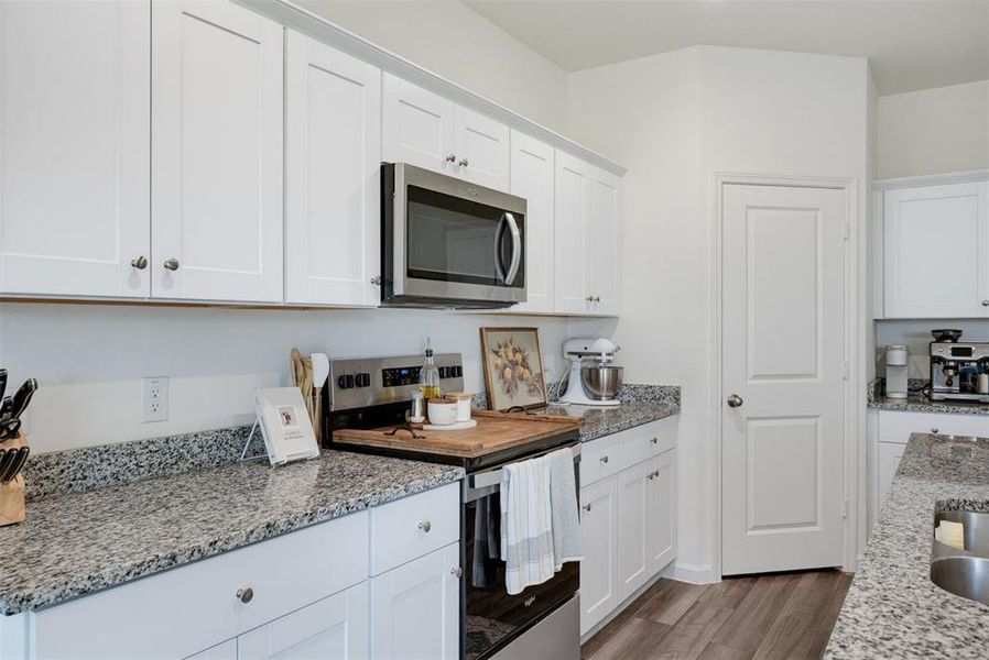 Kitchen featuring white shaker-style cabinetry, stainless steel microwave, and granite countertops