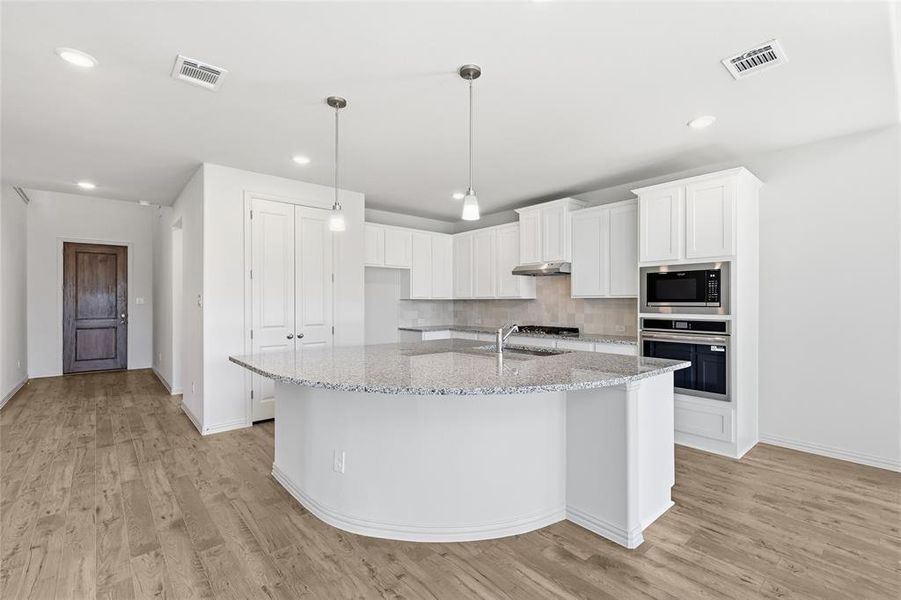 Kitchen with white cabinets, stainless steel appliances, pendant lighting, decorative backsplash, and light stone counters