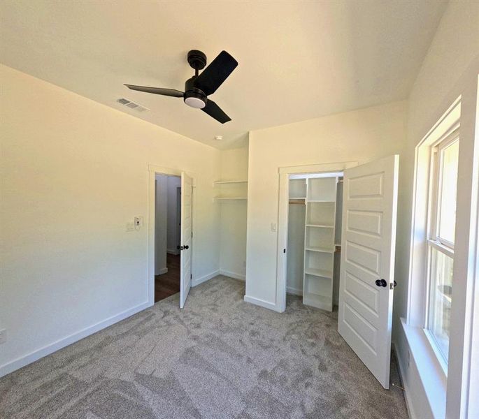 Unfurnished bedroom with carpet, a ceiling fan, and a walk in closet Unfurnished bedroom with carpet, a ceiling fan, and a walk in closet