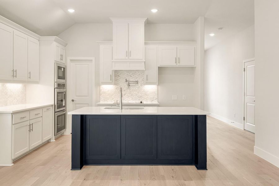 White kitchen with navy blue island, white quartz countertops, tile backsplash, and light hardwood floors