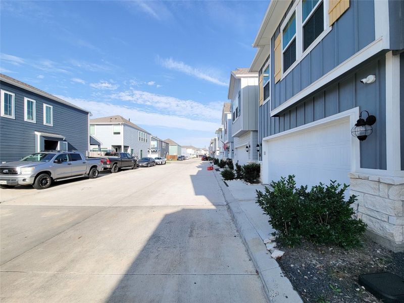 Modern townhomes line a clean, quiet street with neatly maintained exteriors and driveways. The area is well-kept and features ample parking.