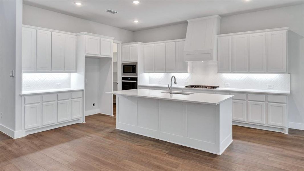 Kitchen with a kitchen island with sink, light hardwood / wood-style flooring, stainless steel appliances, and custom exhaust hood