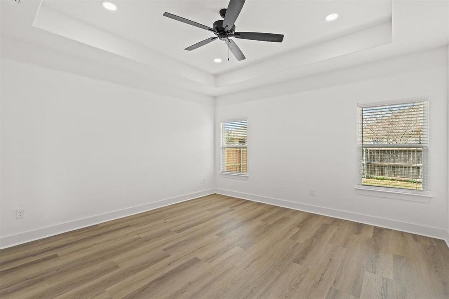 Unfurnished room with ceiling fan, light wood finished floors, recessed lighting, and a tray ceiling