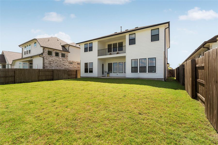 A fenced backyard offers ample green space and a covered patio with a second-story balcony above. A fenced backyard offers ample green space and a covered patio with a second-story balcony above.