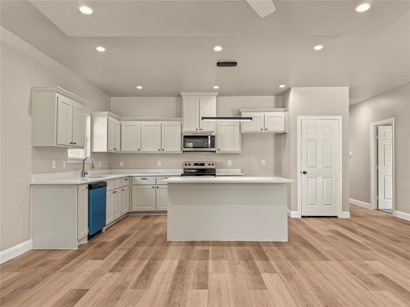 Spacious kitchen featuring white cabinetry, light-toned countertops, a central island, stainless steel appliances, and wood-finish flooring Spacious kitchen featuring white cabinetry, light-toned countertops, a central island, stainless steel appliances, and wood-finish flooring