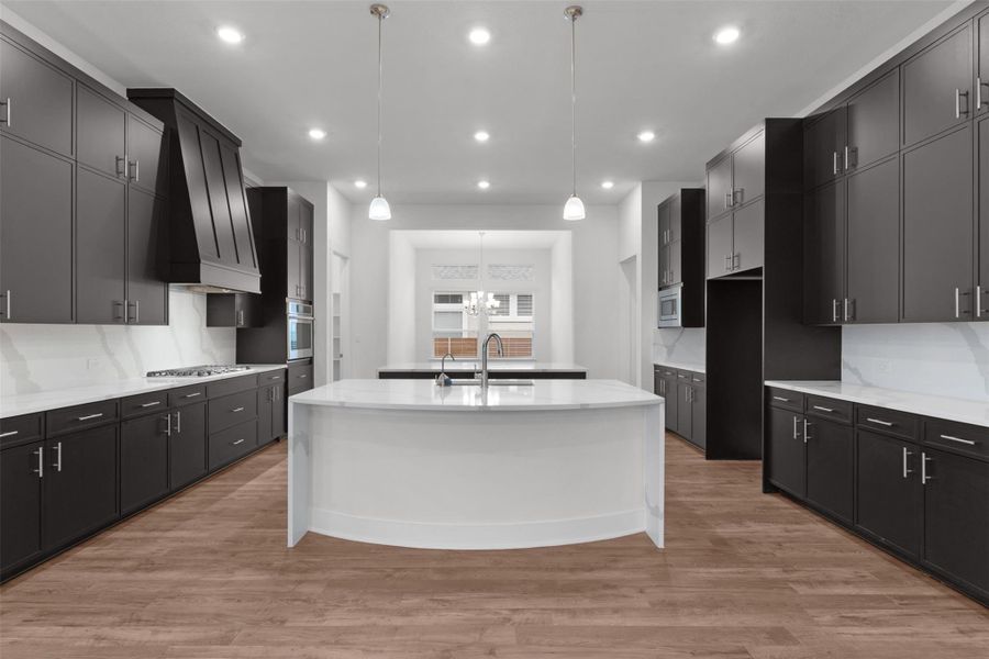 Kitchen featuring decorative light fixtures, light stone countertops, a center island with sink, light wood-type flooring, and custom exhaust hood