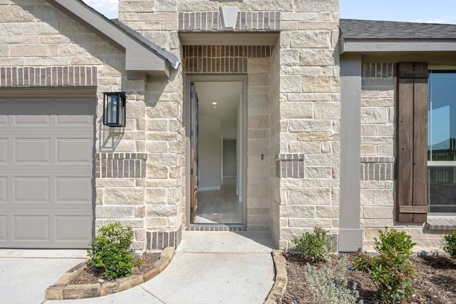 Home entrance with stone exterior, open front door, wall sconce, and attached garage nearby